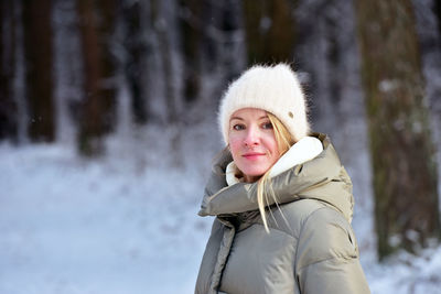 Portrait of smiling young woman standing in forest during winter