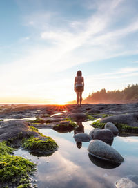 Rear view of woman standing on rock against sky during sunset