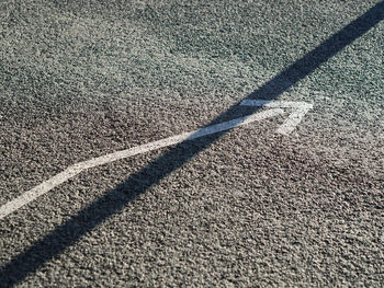 High angle view of arrow sign and long shadow on road