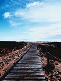 Boardwalk leading towards sea against sky