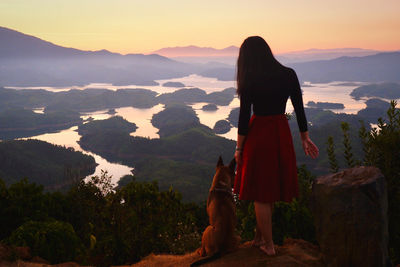 Rear view of woman standing against lake and mountains with her dog