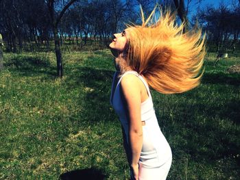 Side view of beautiful young woman with tousled hair standing on field