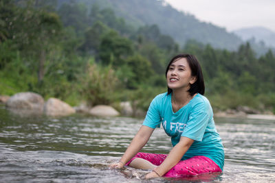 Smiling young woman sitting against water