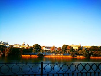 Buildings by river against clear blue sky