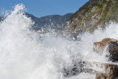 Sea waves splashing on mountain against sky