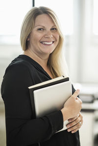 Portrait of happy businesswoman holding book and digital tablet in creative office