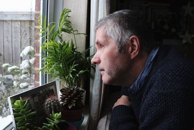 Close-up of man looking through window at home