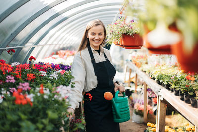 Portrait of a young gardener woman watering flowers in a greenhouse. daily care of plants