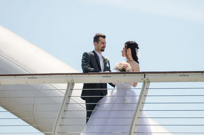 Wedding couple standing by bridge railing against clear sky