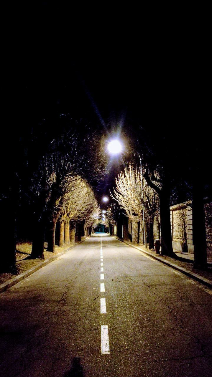EMPTY ROAD ALONG ILLUMINATED STREET LIGHTS IN CITY