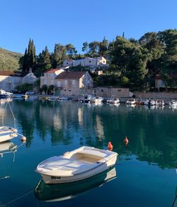 Boats moored in safe harbour with  turquoise water, buildings against clear sky