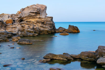 Rocks in sea against clear blue sky