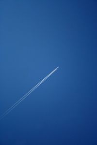 Low angle view of vapor trails against clear blue sky