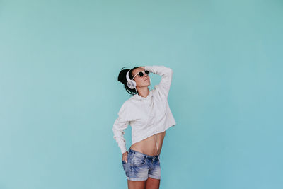 Young woman wearing sunglasses standing against blue background