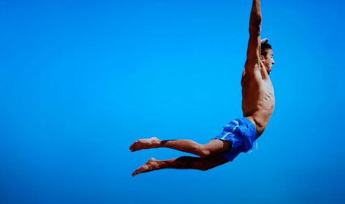 Shirtless man jumping against clear blue sky