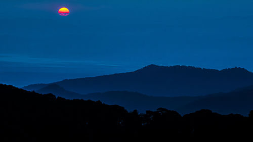 Scenic view of silhouette mountains against blue sky at night