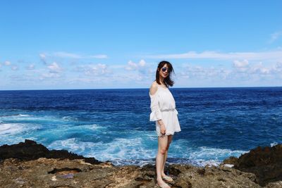 Young woman standing at sea shore against sky