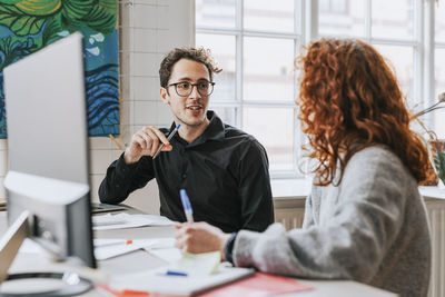 Businessman discussing with female redhead colleague at desk in office