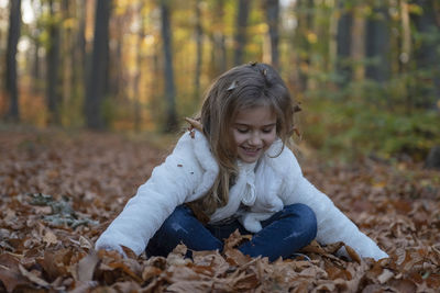 Smiling girl playing with dry leaves on field in forest