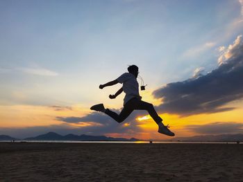 Man jumping in sea against sky during sunset