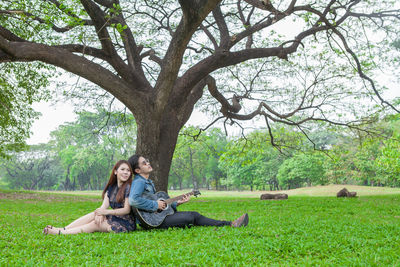 Rear view of woman sitting on grassland against trees