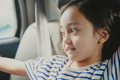 Young little girl enjoying the trip in back seat looking out the window of the car
