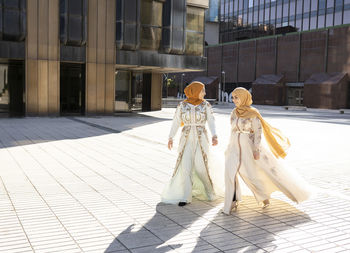 Female friends wearing hijabs and dress walking on footpath during sunny day