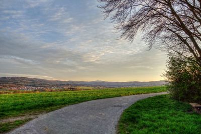 Road passing through field against cloudy sky