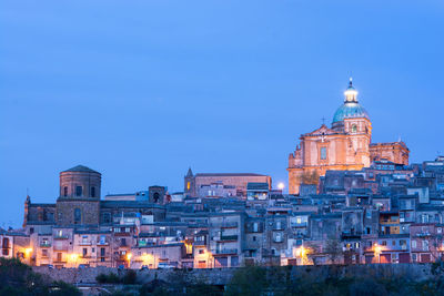 Illuminated buildings in city against clear blue sky