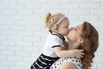 Side view of mother kissing daughter against wall