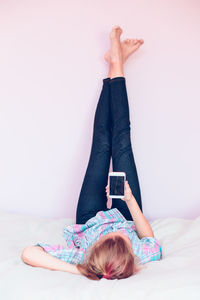 Teenage girl holding mobile phone while lying on bed at home