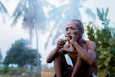 Shirtless man smoking while sitting outdoors