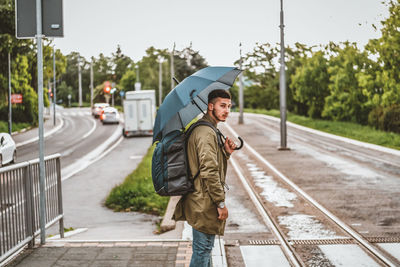 Man with umbrella  on a rainy day. handsome young tourist with backpack is crossing the road