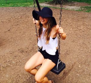 Smiling young woman sitting on swing at park