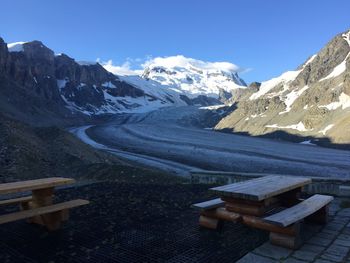 Empty benches and tables by dirt road against snowcapped mountains