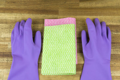 High angle view of purple gloves with cleaning equipment on wooden table