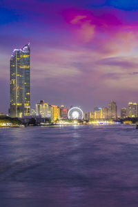 Illuminated buildings in city against cloudy sky