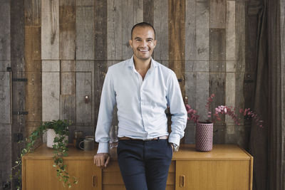 Portrait of happy businessman leaning on sideboard against wood paneling in portable office truck