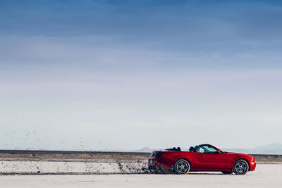 Red car on shore against sky