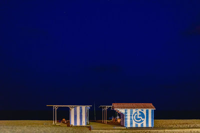 Hooded beach chairs against clear blue sky at night