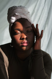 Graceful young overweight african female in traditional turban touching face with closed eyes in sunlight