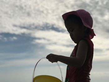 Girl playing with bucket while sitting at beach