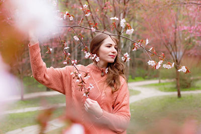 Woman standing under pink blossom branch sakura in park