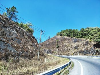 Road by trees against clear blue sky