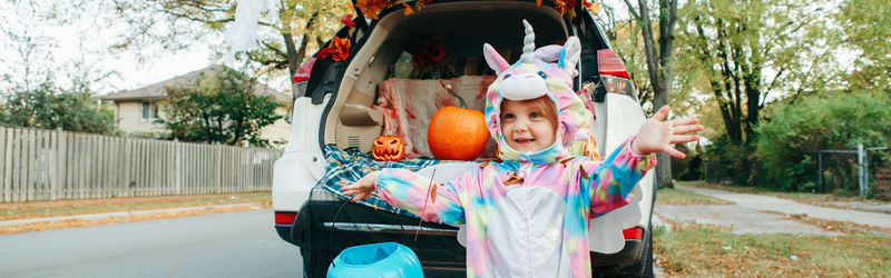 Cute girl wearing costume standing by car trunk