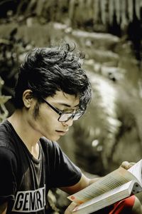 Young man reading book while sitting outdoors