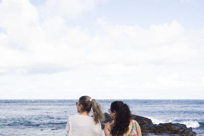 Mother and daughter sitting on the pier of the port of barra facing the sea. 