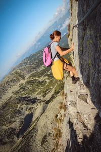 Side view of woman climbing on mountain against sky