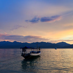 Boat moored in sea against sky during sunset