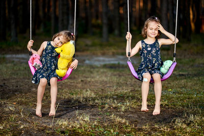 Portrait of cute girls sitting on swing at park